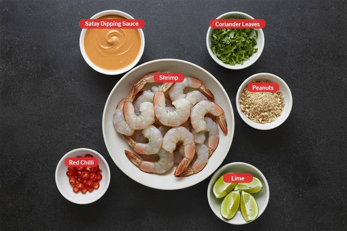 Top shot of ingredients: stay dipping sauce, coriander leaves, shrimp, peanuts, lime, and red chilli.