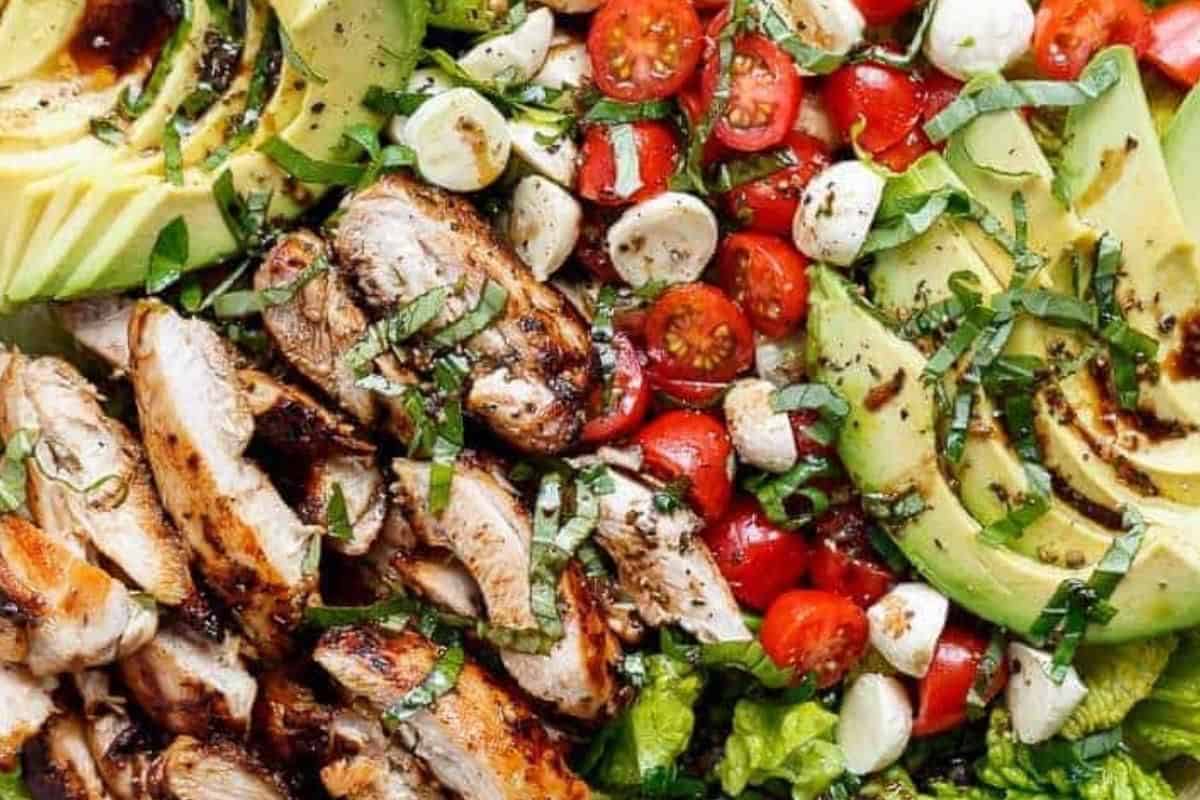 Slice the chicken into strips and combine it with the lettuce, avocado, tomatoes and mozzarella in a large bowl. Drizzle dressing, and add basil leaves and season with salt and pepper.