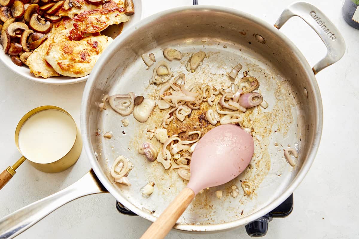 Add sliced shallots to the pan and pour in champagne to deglaze, scraping up any browned bits.