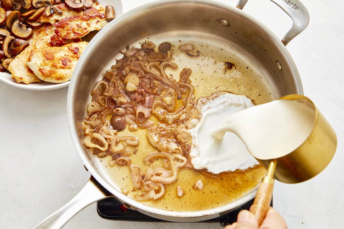 Pouring cream into the pan with sautéed shallots and champagne.