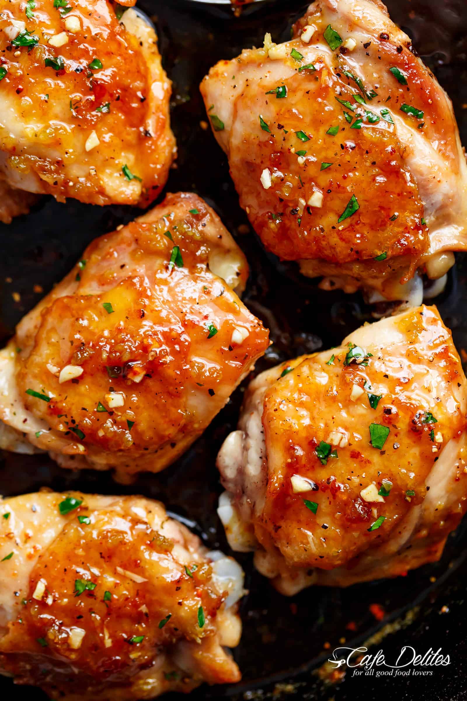 Chicken glazed in honey garlic sauce in a pan, with chopped, fresh herbs on top. 