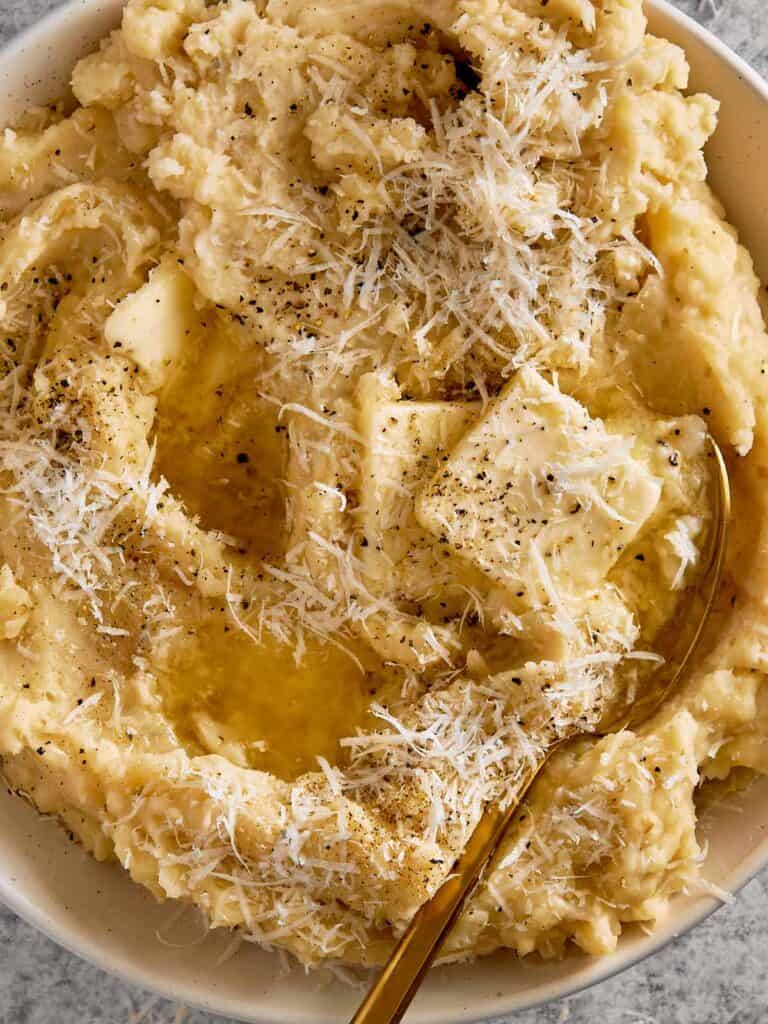 top down view of a white bowl filled with creamy potatoes and two cubes of butter with herbs on top close up shot - 11