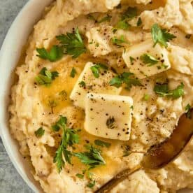 top down view of a white bowl filled with creamy potatoes and two cubes of butter with herbs on top close up shot with chives on top - 13