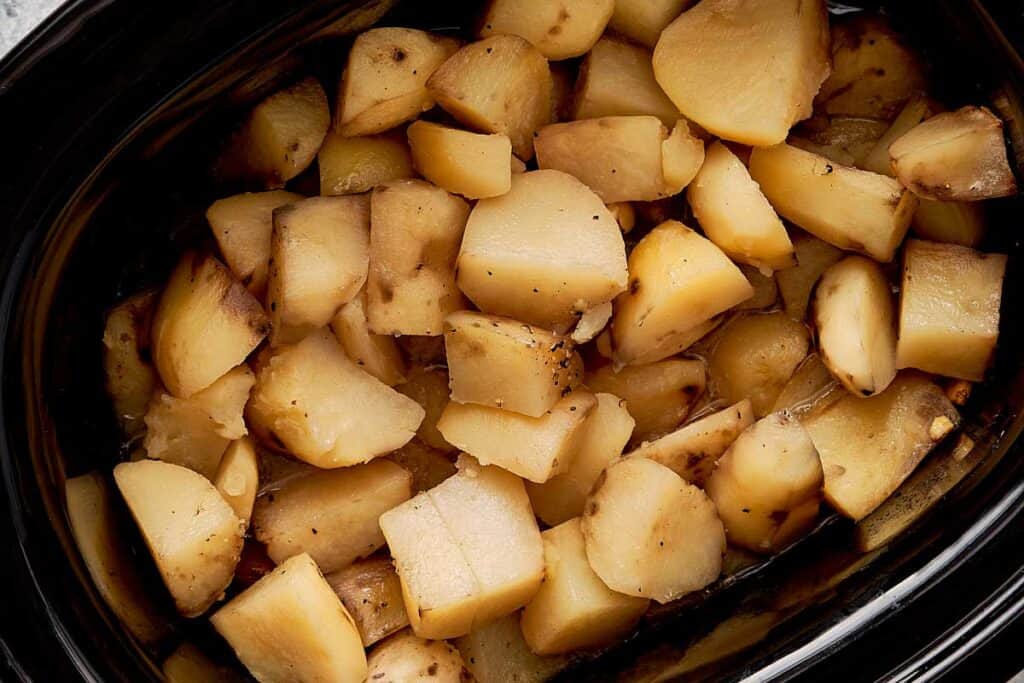a top down view of cut up baby potatoes inside a slow cooker - 4