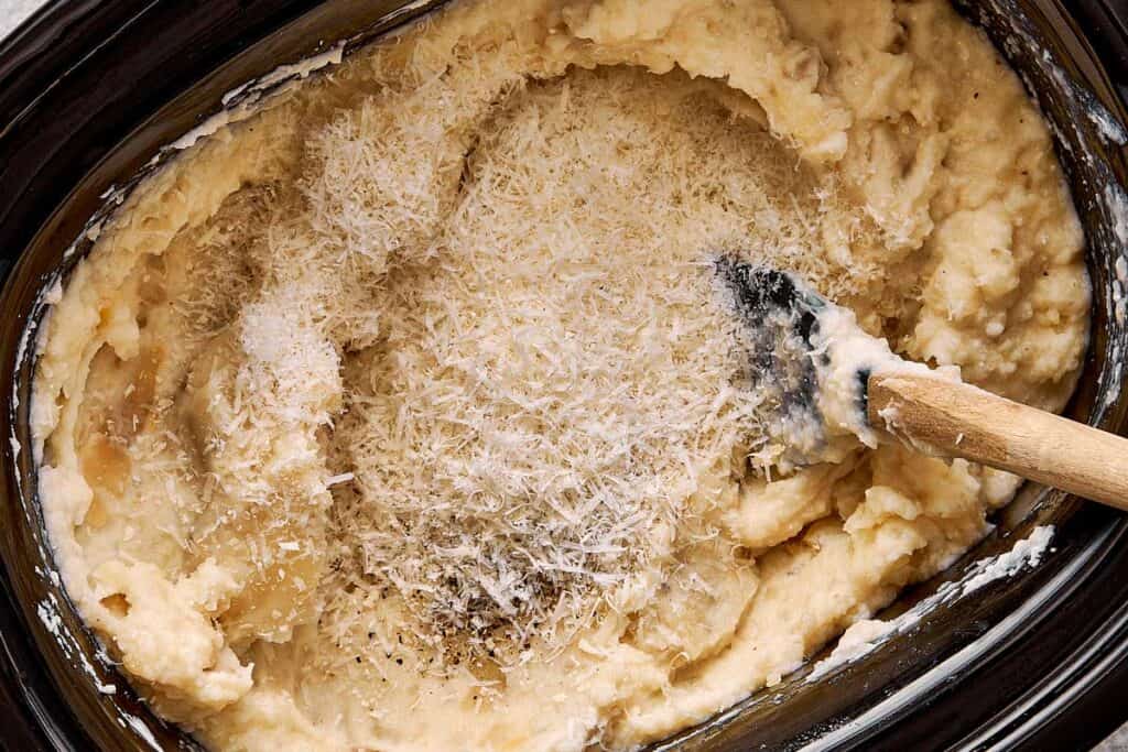 a top down view of mashed potatoes very creamy stirred by a wooden spoon in a slow cooker with parmesan cheese on top - 9