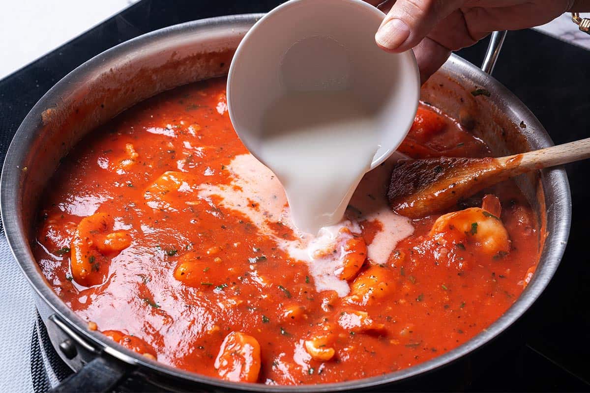 rich red sauce in a skillet with cream being poured in