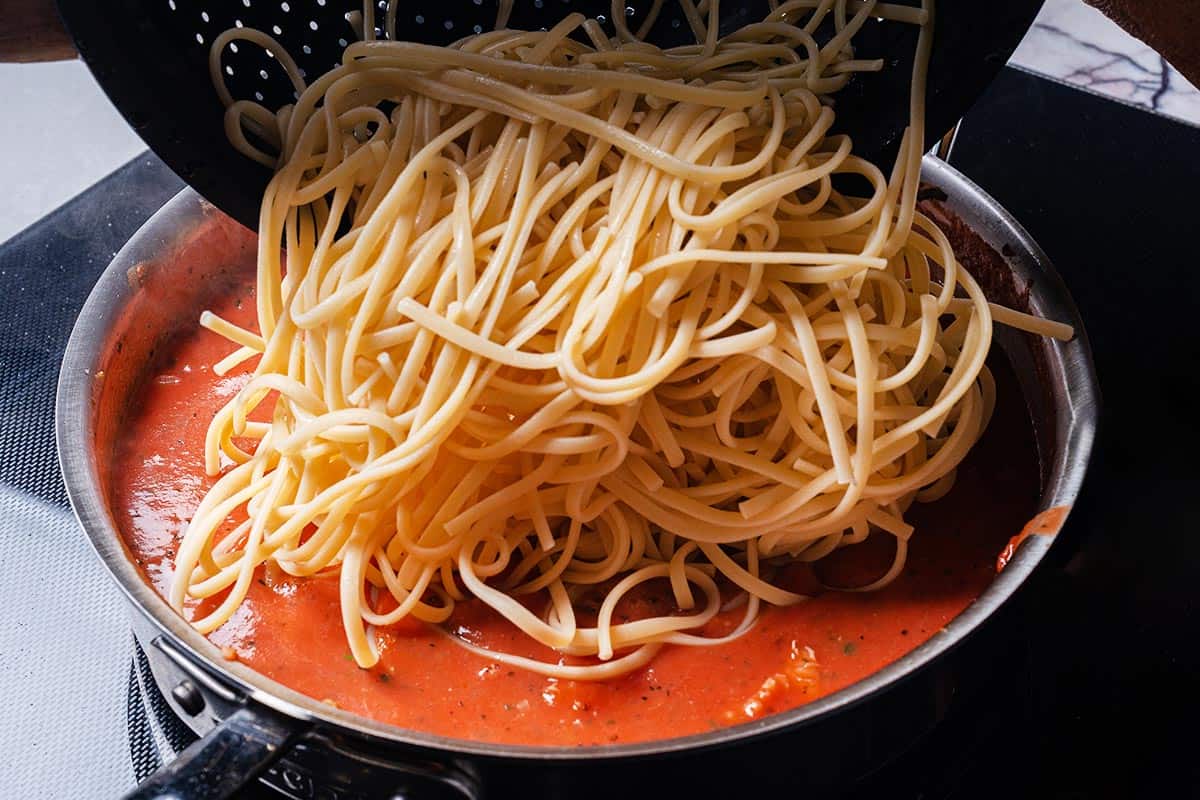 pasta being poured into a rich red sauce