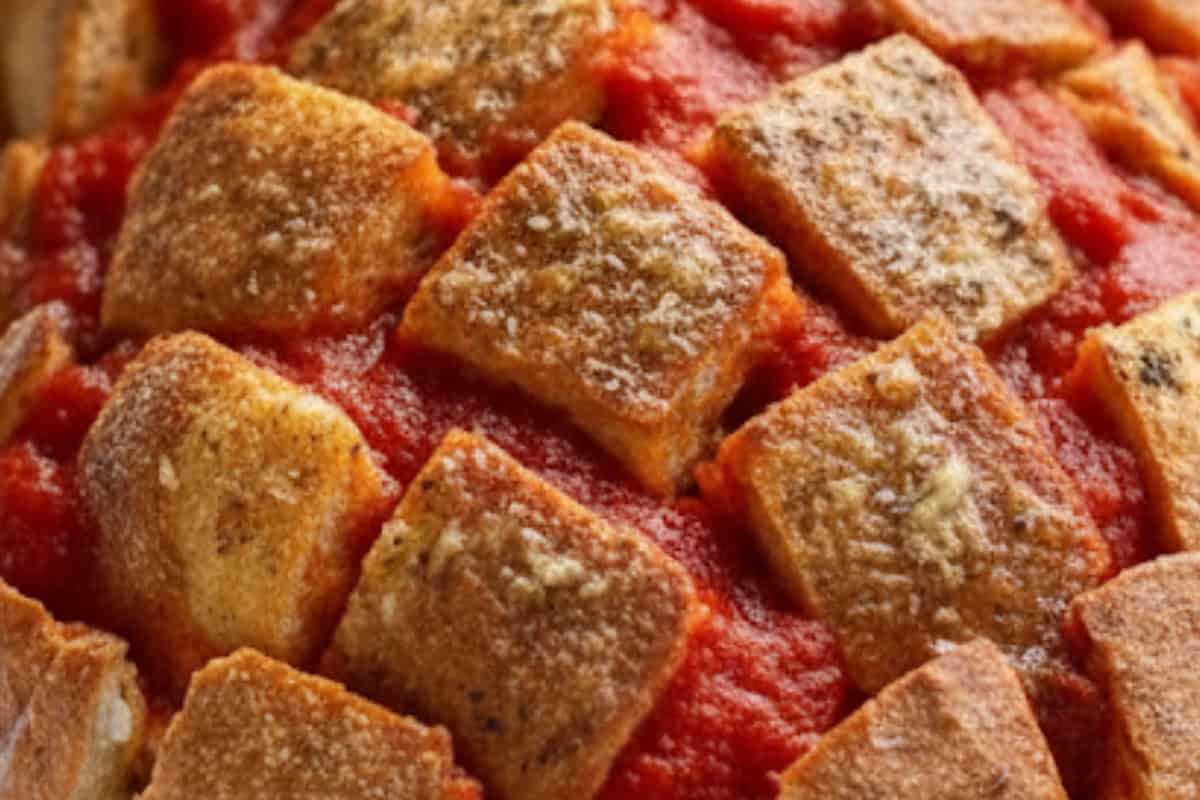 Transfer the loaf to the lined tray. Drizzle half the garlic butter into the cuts, then spoon in pizza sauce to lightly coat.