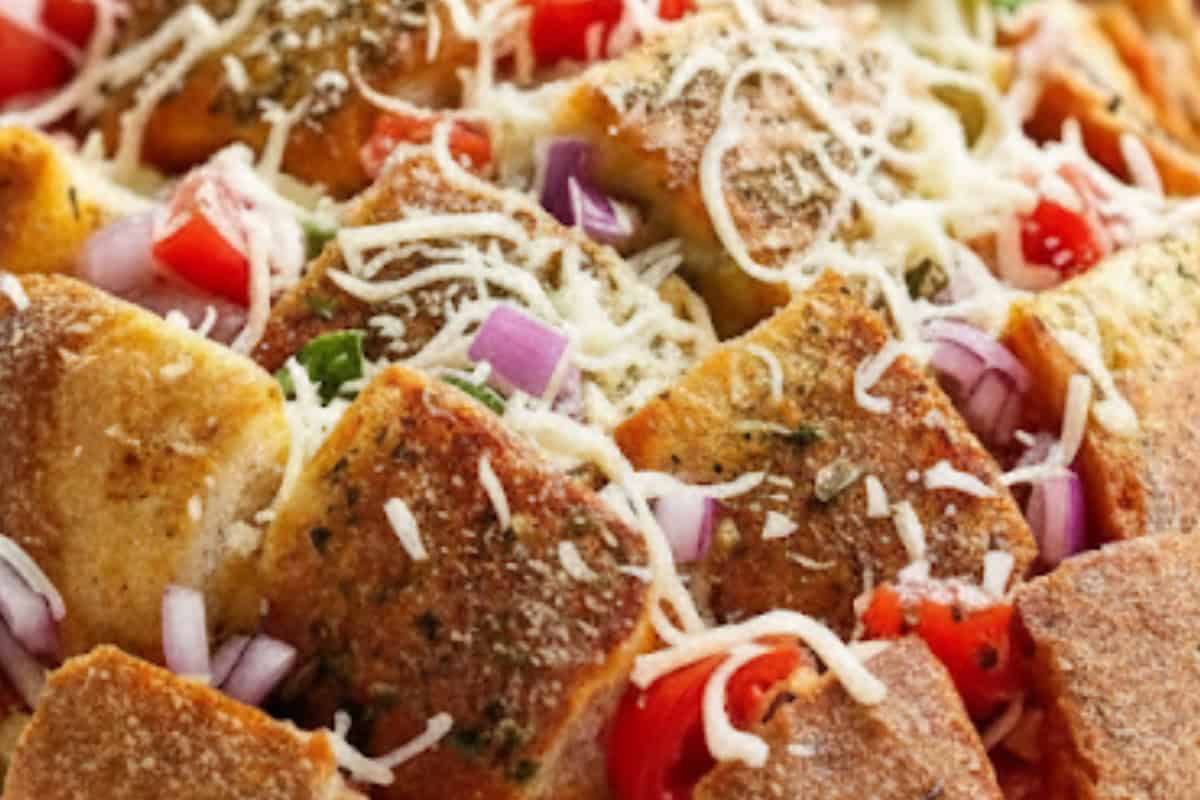 Tuck onion, tomato, mini pepperoni, and basil throughout the cuts. Sprinkle mozzarella over and into gaps 