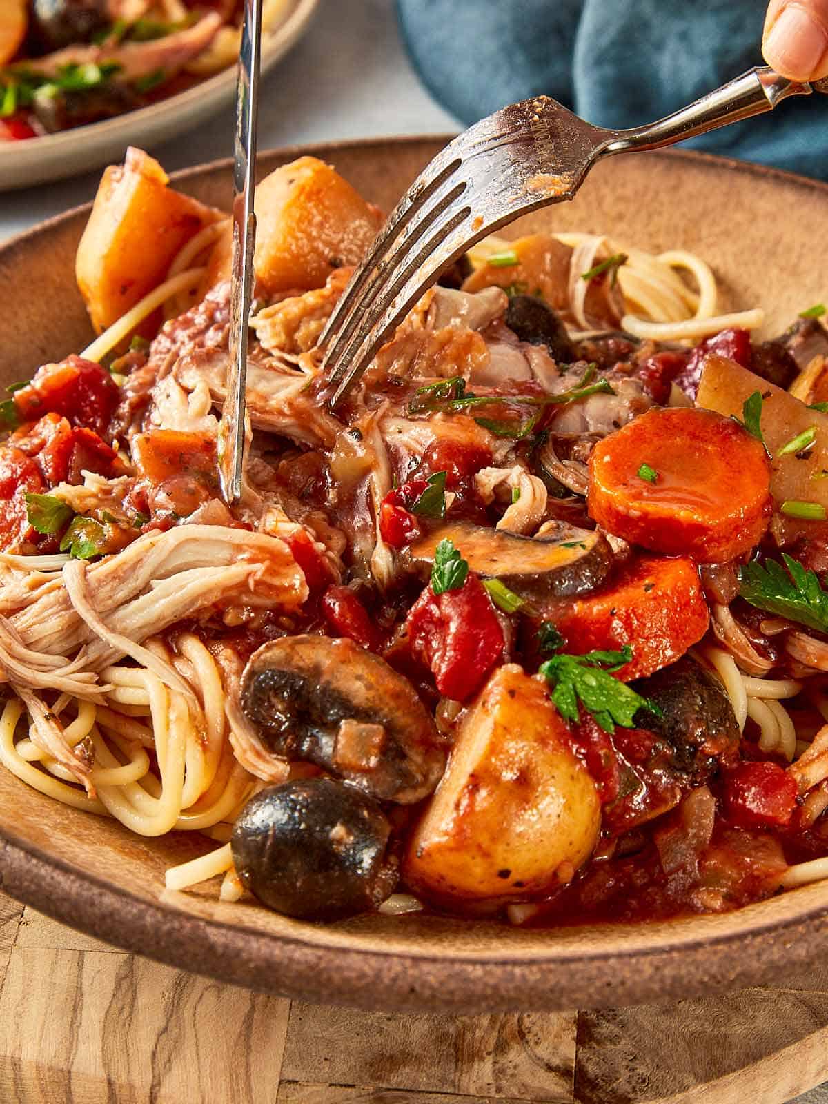 Slow cooker chicken cacciatore served over spaghetti with tender shredded chicken, potatoes, mushrooms, and carrots in a tomato sauce
