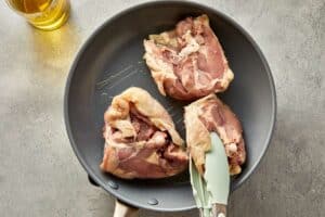 Bone-in chicken thighs searing skin-side down in a skillet
