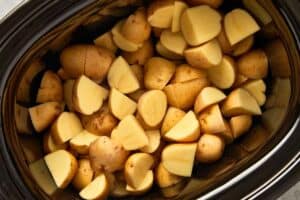 Quartered baby potatoes layered in the bottom of a slow cooker