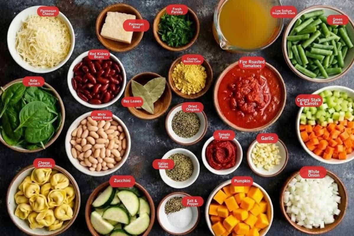 Flat lay photo of ingredient shot, of parmesan cheese, parmesan rind fresh parsley, low sodium vegetable stock, green beans, celery stalks and carrots, garlic, white onion, pumpkin, salt and pepper Italian herb, tomato paste, dried oregano, bay leaves, zucchini, cheese tortellini, baby spinach, red kidney beans, white kidney beans, crushed bouillon cubes, tomato paste, fire roasted tomatoes