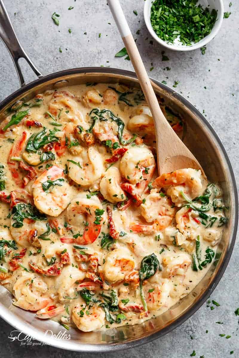 Creamy Garlic Butter Tuscan Shrimp coated in a light and creamy sauce filled with garlic, sun dried tomatoes and spinach! Packed with incredible flavours! | https://cafedelites.com