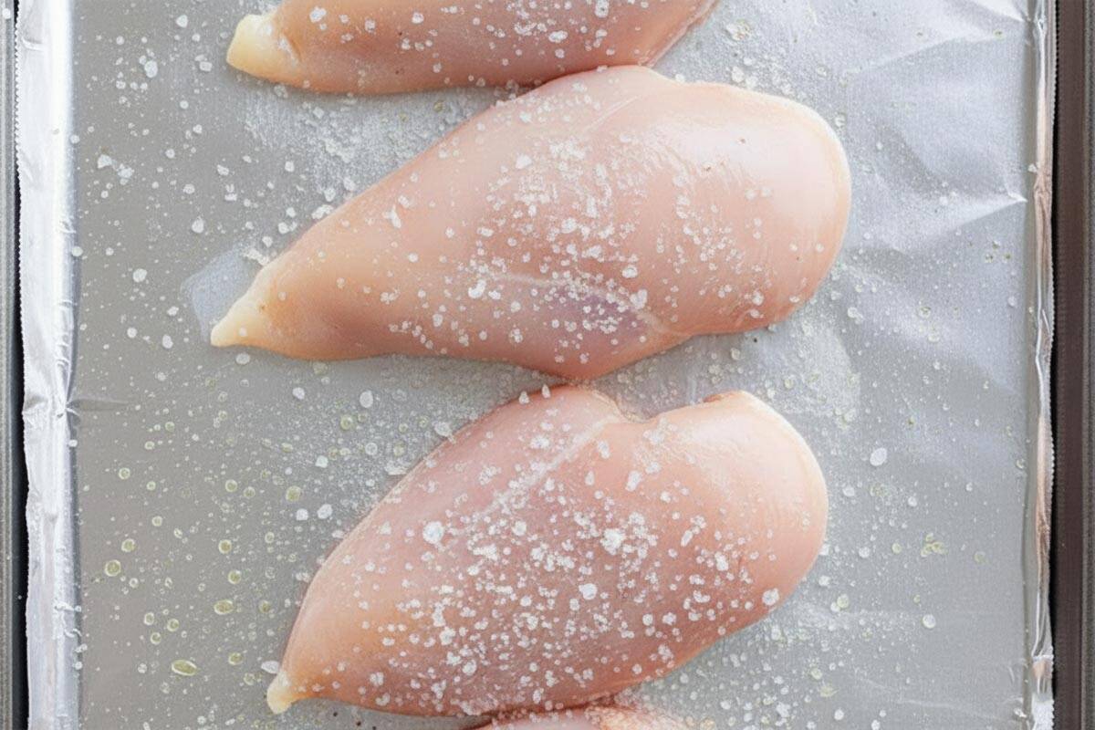 Chicken breasts on a tray seasoned with salt.