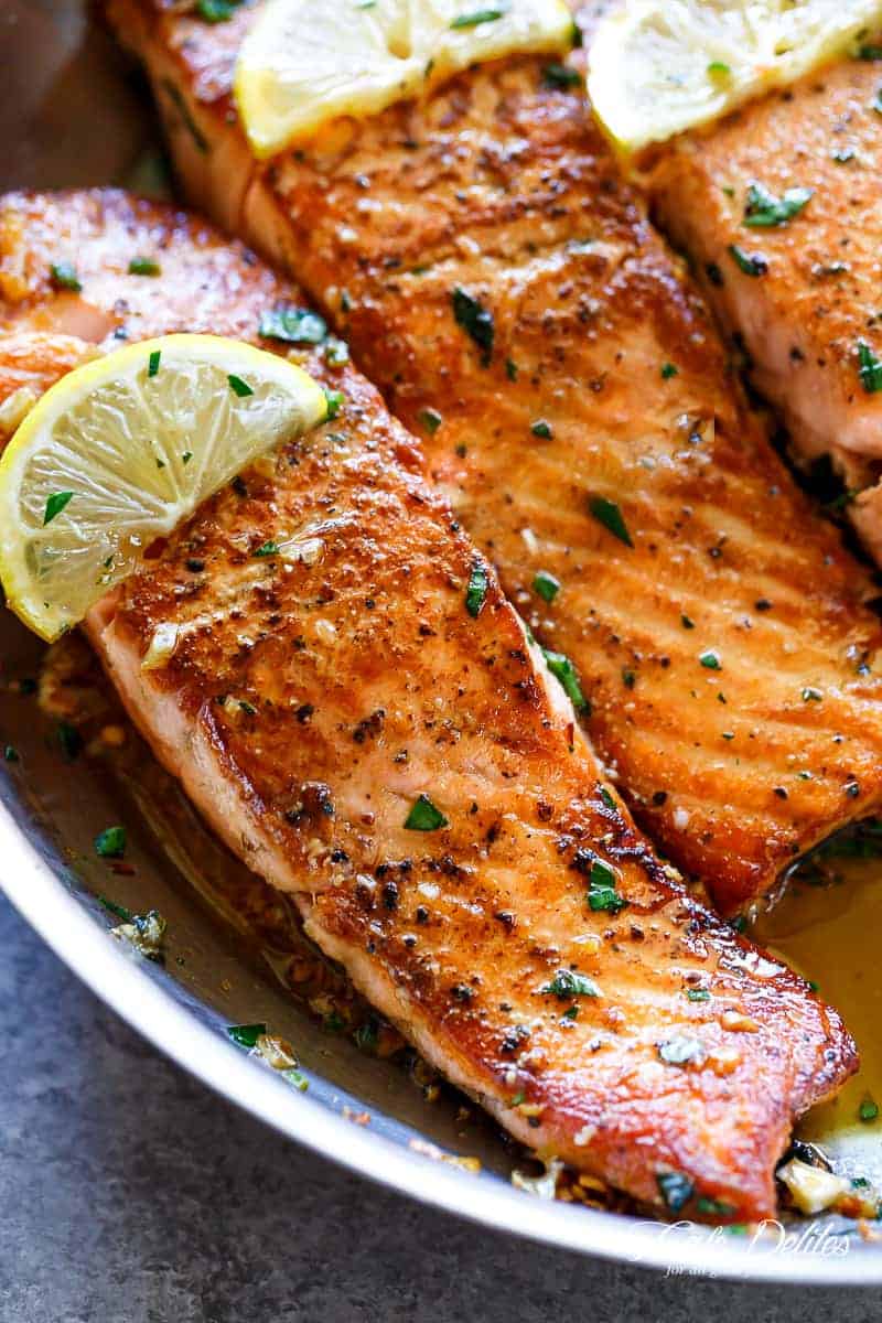 Close up of salmon in pan with lemon and herbs on top. 