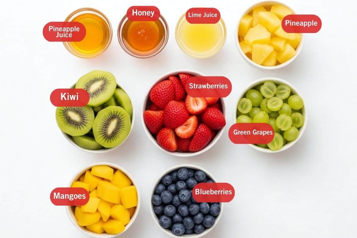 Flat lay photo of ingredient shot of pineapple juice, honey, lime juice, pineapple, kiwi, strawberries, green grapes, mangoes, blueberries
