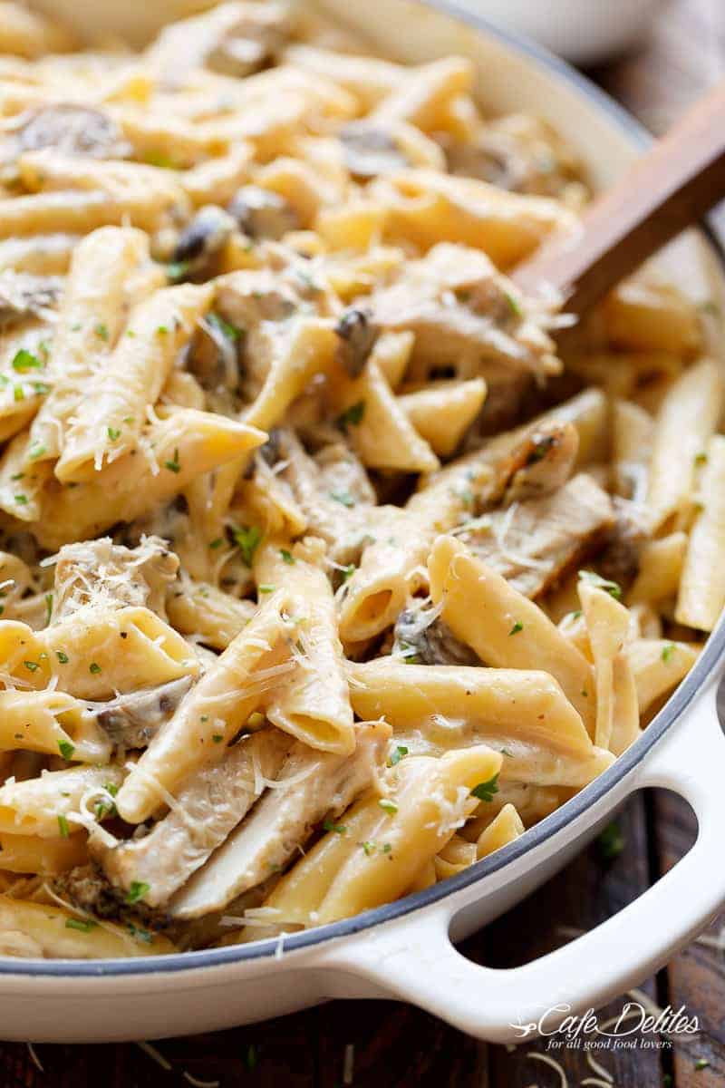 Seared chicken strips mixed through this One-Pot Creamy Mushroom Chicken Pasta, with garlic, mushrooms AND parmesan cheese with fresh herbs sprinkled over the top. I wooden spoon is mixing the pasta in a le creuset pot. 