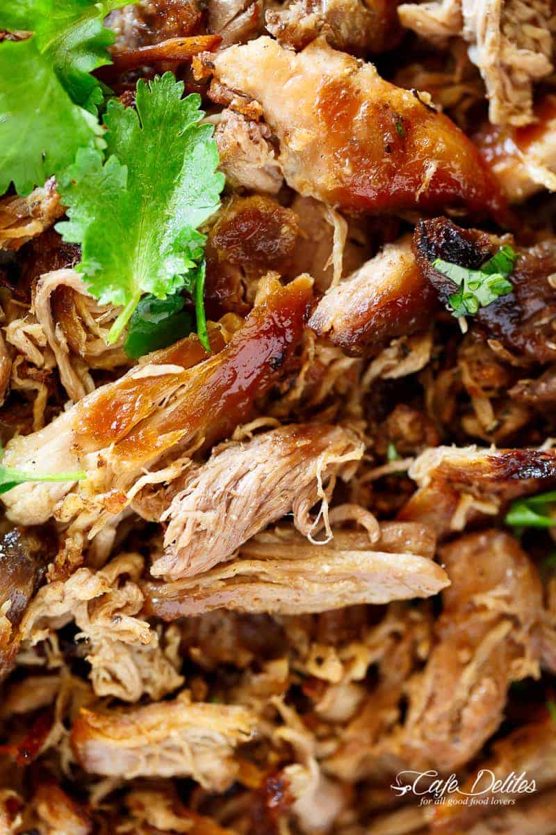 Close up image of pulled pork with fresh cilantro and parsley leaves on top. 