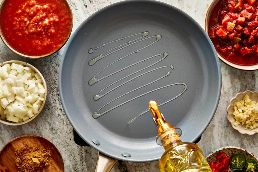 a top down view of a pan with oil being poured into it and bowl of ingredients around the outside of the pan - 5