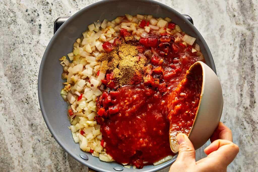 a top down view of a pan frying diced up vegetables and a grey bowl of tomato salsa being poured in the middle of the pan - 7
