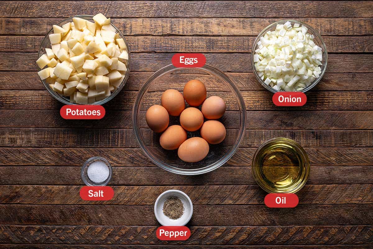 ingredients laid out against a woodgrain background from top view. Potatoes, egg, onion, salt, pepper, oil
