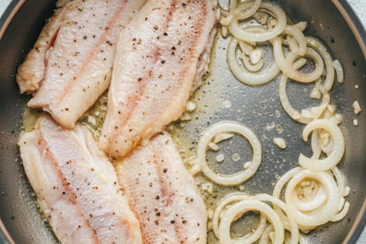 Pushed the fish gently to one side of the pan and add the garlic and onion on the other side.