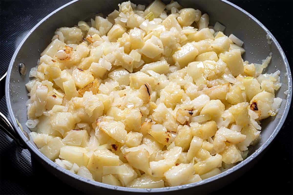 potatoes and onion close up in a pan being fried