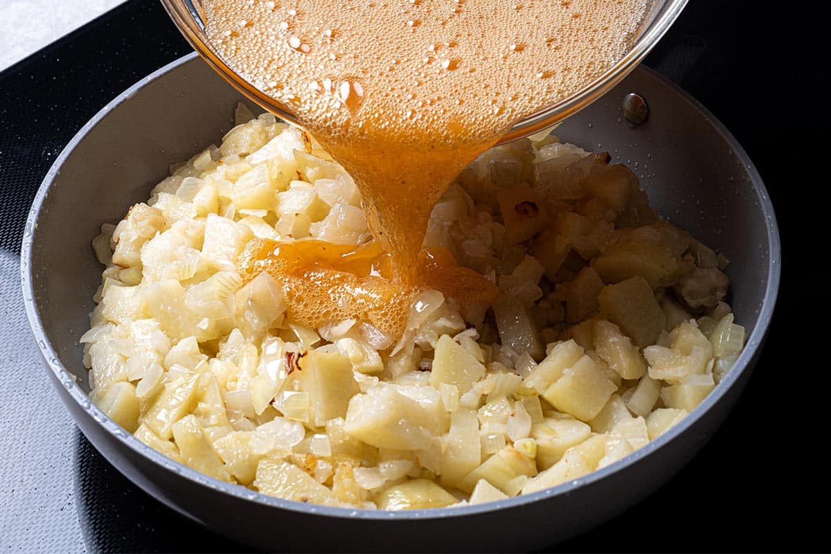 fried potatoes and onion close up in a pan with an egg mixture being poured in