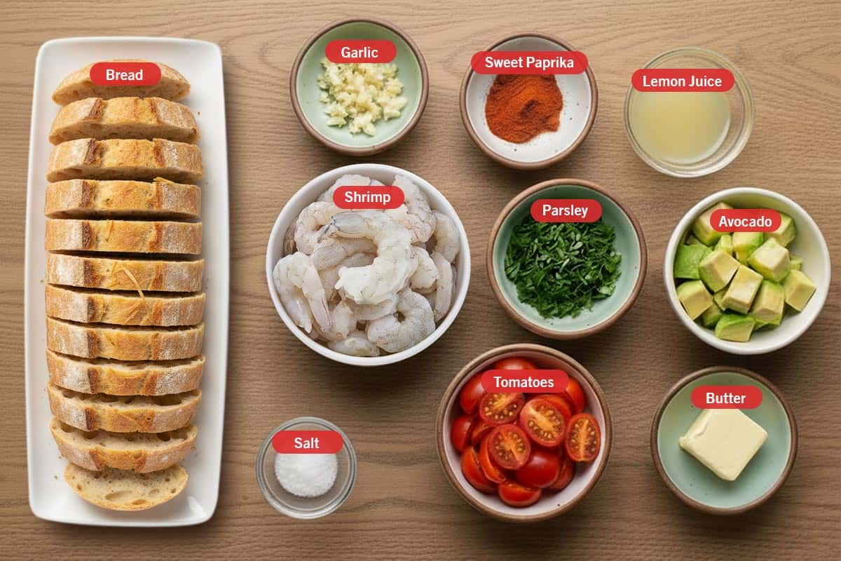 Top shot of ingredients: bread, garlic, sweet paprika, lemon juice, shrimp, parsley, avocado, salt, tomatoes, butter.
