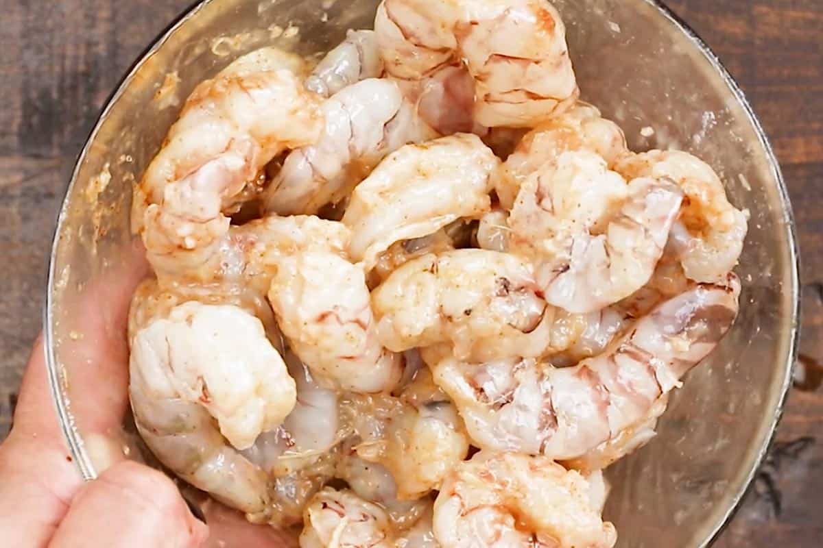 Combining garlic, paprika, lemon juice, and shrimp in a bowl.