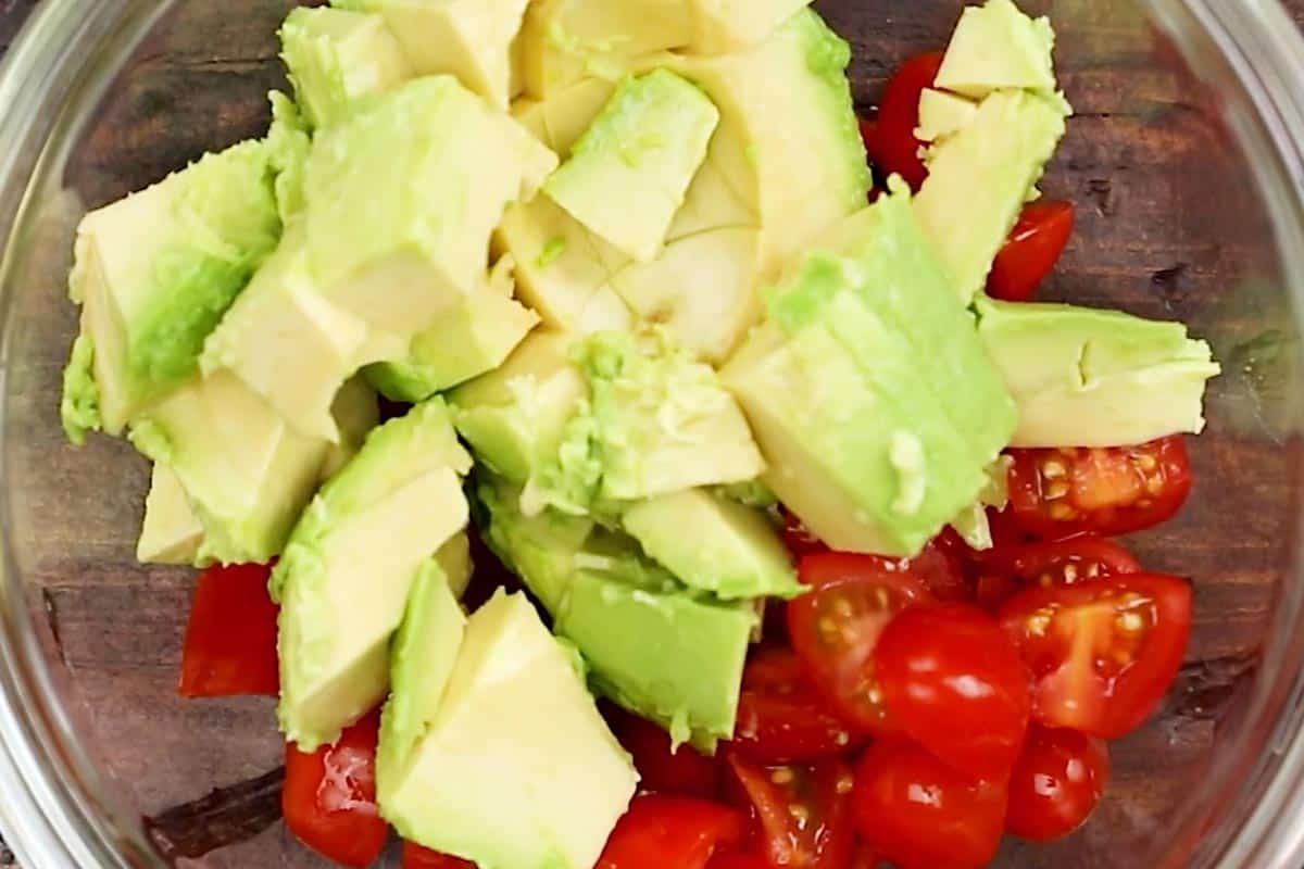 Combining cubed avocado, halved tomatoes in a bowl.