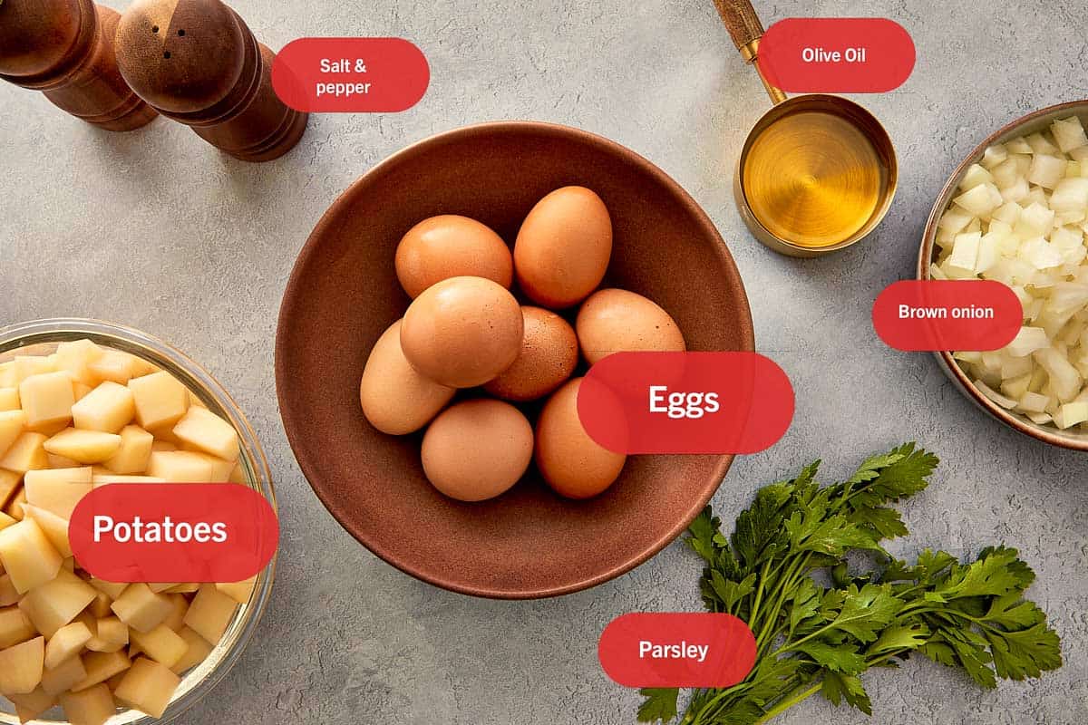 Ingredients for Spanish Omelette (Tortilla Española) including eggs, diced potatoes, onion, olive oil, salt, pepper, and parsley laid out on a surface.