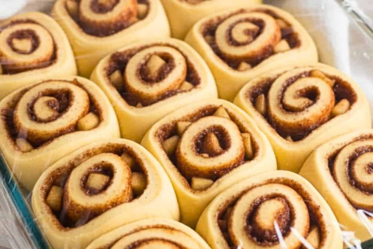 Starting from a long edge, roll the dough tightly like a jelly roll and pinch the seam to seal. Trim the ends, slice into twelve 2-inch pieces, and arrange them in a greased 9×13-inch baking dish.