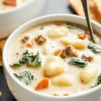 Slow Cooker Creamy Gnocchi Sausage Kale Soup in a medium sized white soup bowl, with spinach, sausage, gnocchi and kale poking through the soup.