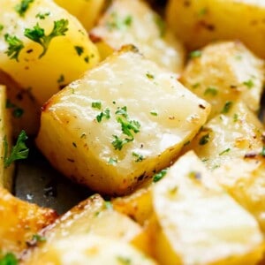 Close up image of Crispy garlic roasted potatoes sprinkled with fresh green herbs on a baking tray.