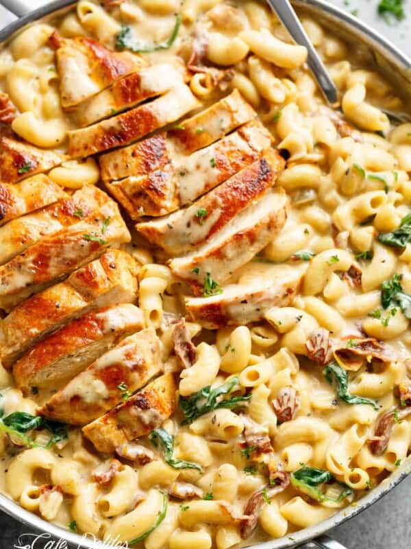 Tuscan chicken sliced, on top of a bed of creamy pasta with sundered tomatoes and spinach with Fresh herbs sprinkled on top.