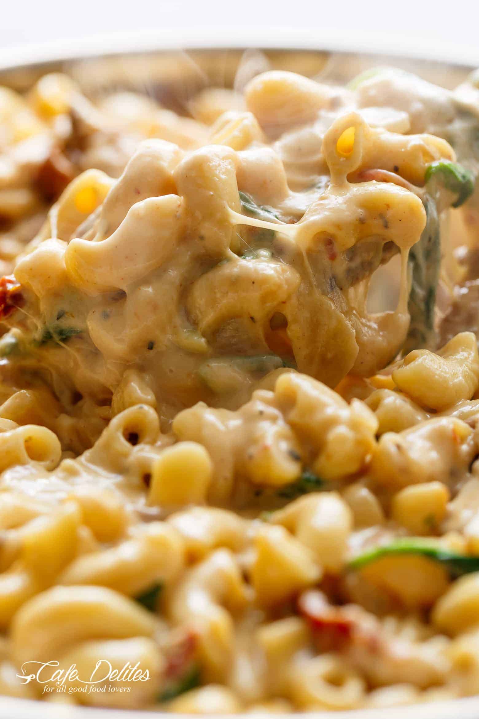 A close up image of steaming hot Tuscan Mac and cheese being scooped up with a serving spoon in a bowl.