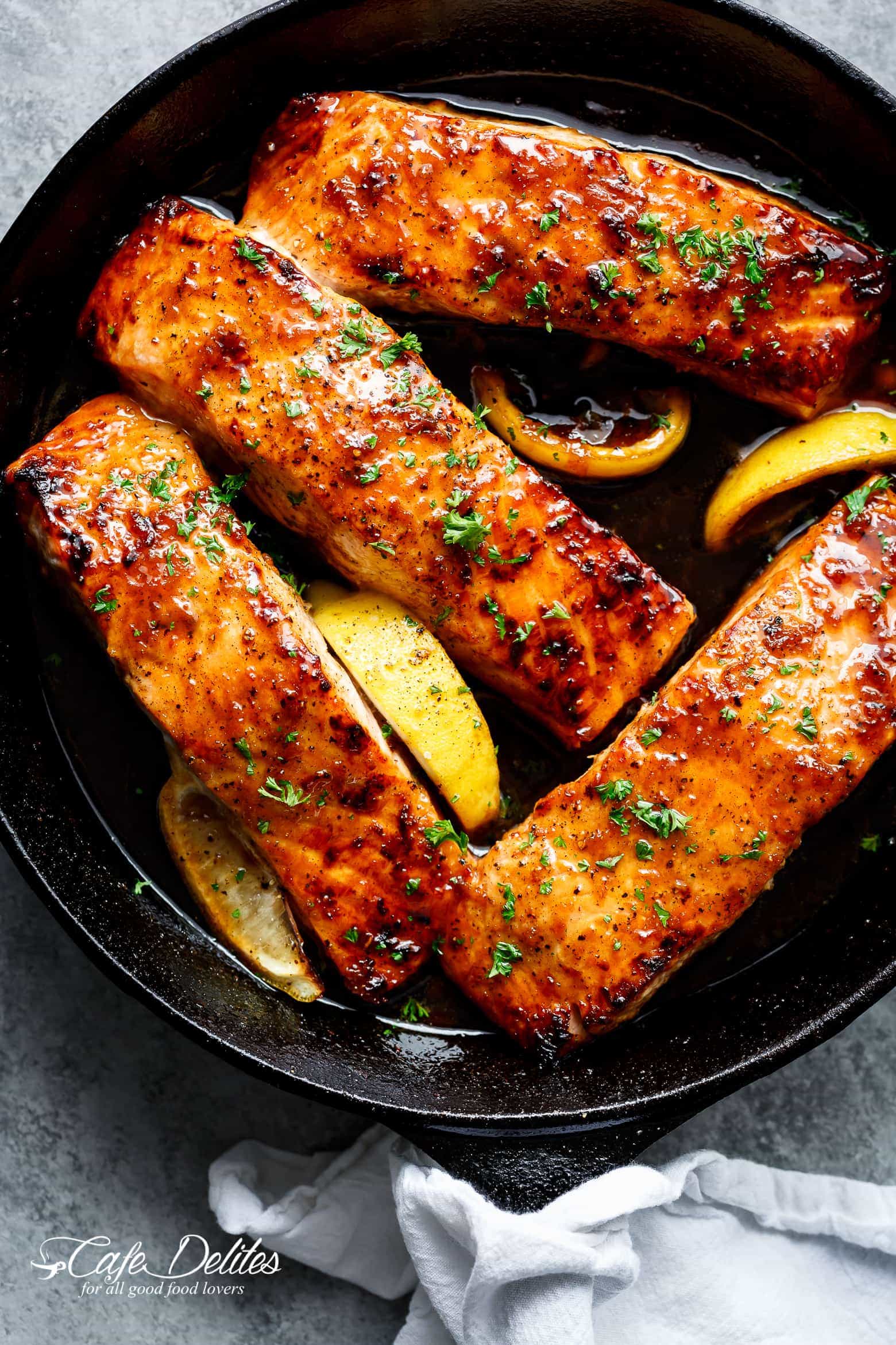 Honey garlic salmon in a black skillet with lemon slices