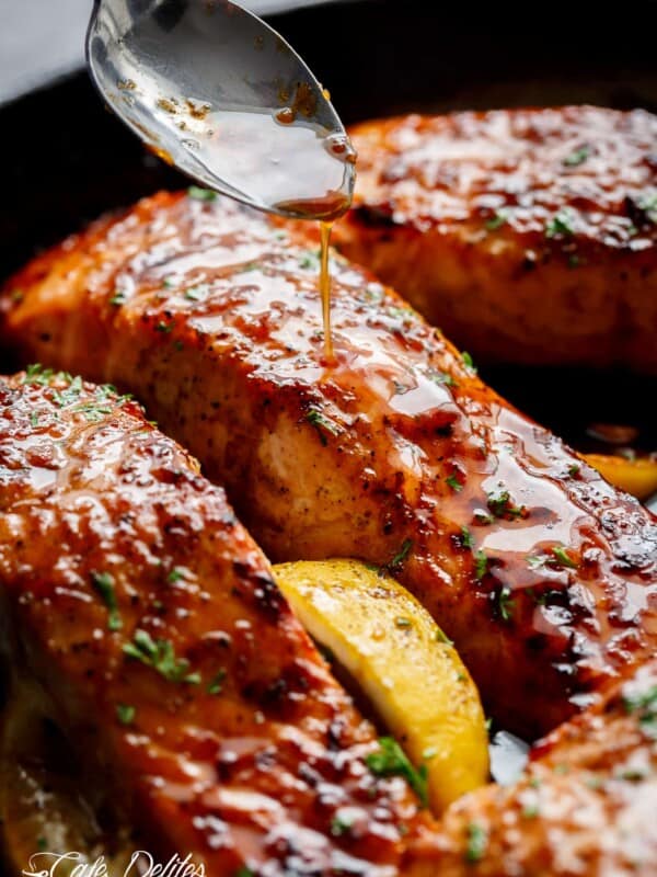 An amazing close-up shot of the salmon fillets coated in honey garlic sauce, sprinkled with basil, and accompanied by a slice of lemon.
