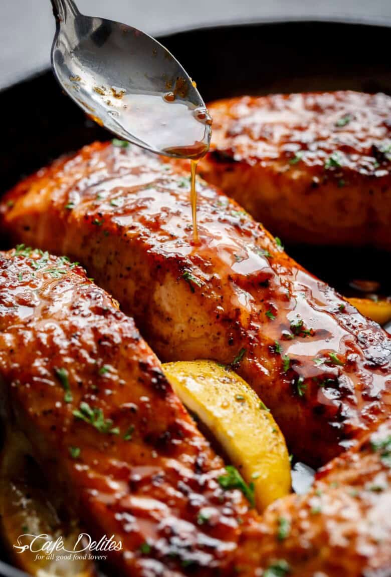 An amazing close-up shot of the salmon fillets coated in honey garlic sauce, sprinkled with basil, and accompanied by a slice of lemon.