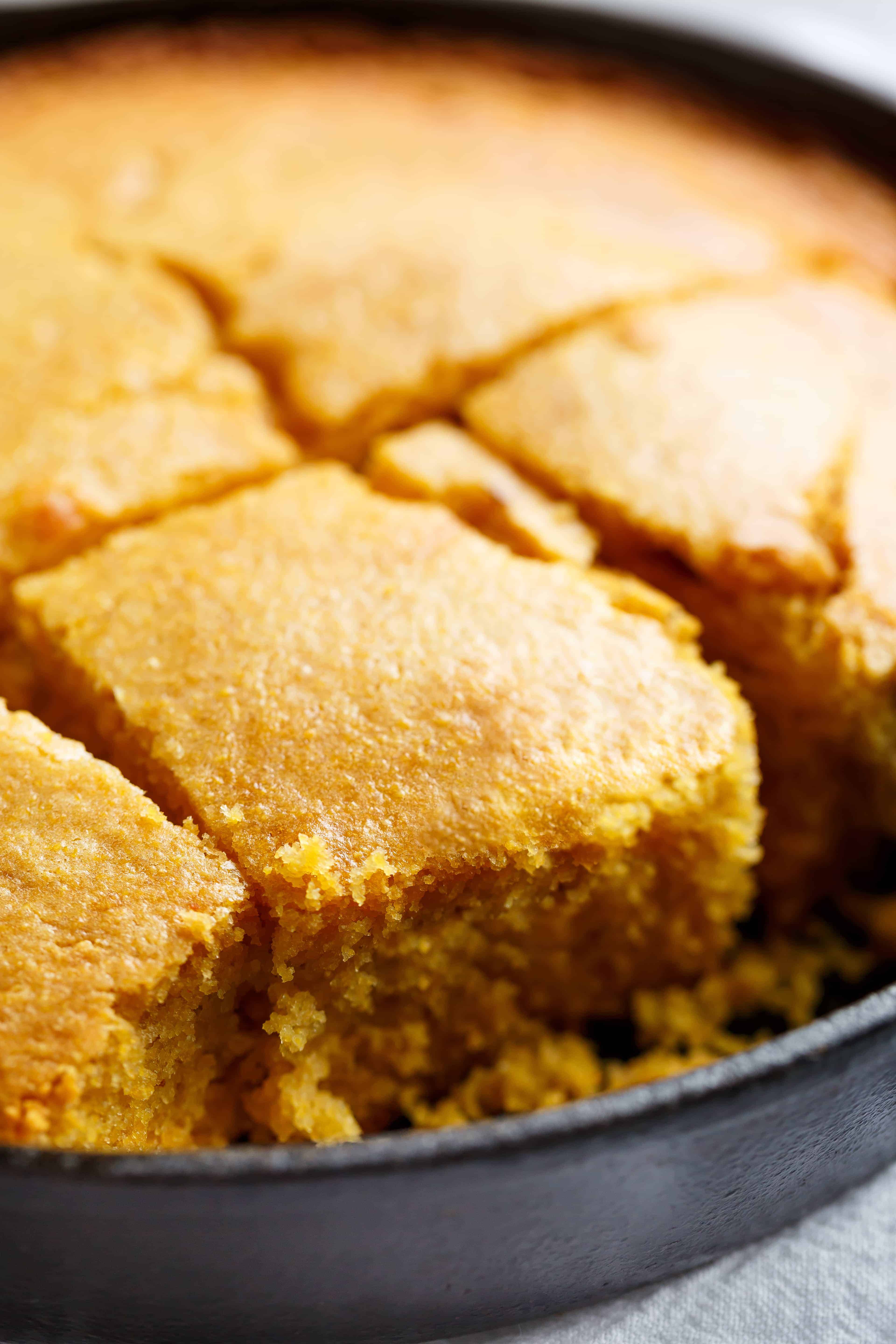 Buttermilk cornbread in a skillet cut into showing the fluffy yellow inside.