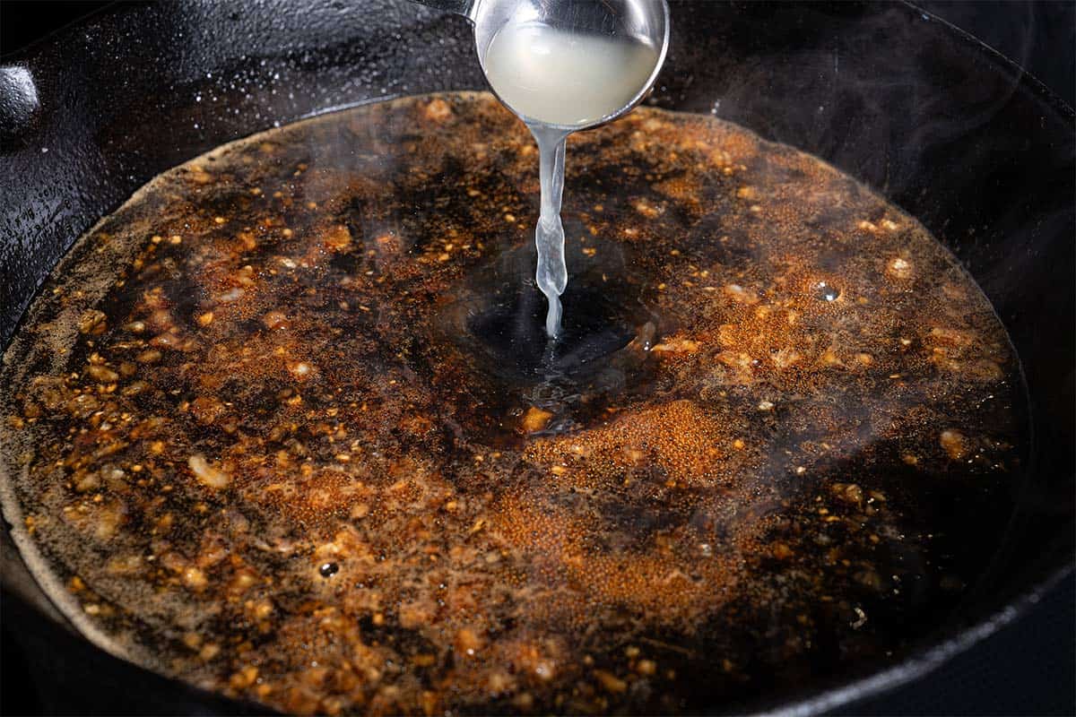 Lemon juice is being added to the skillet where the ingredients are being mixed to create the sauce.