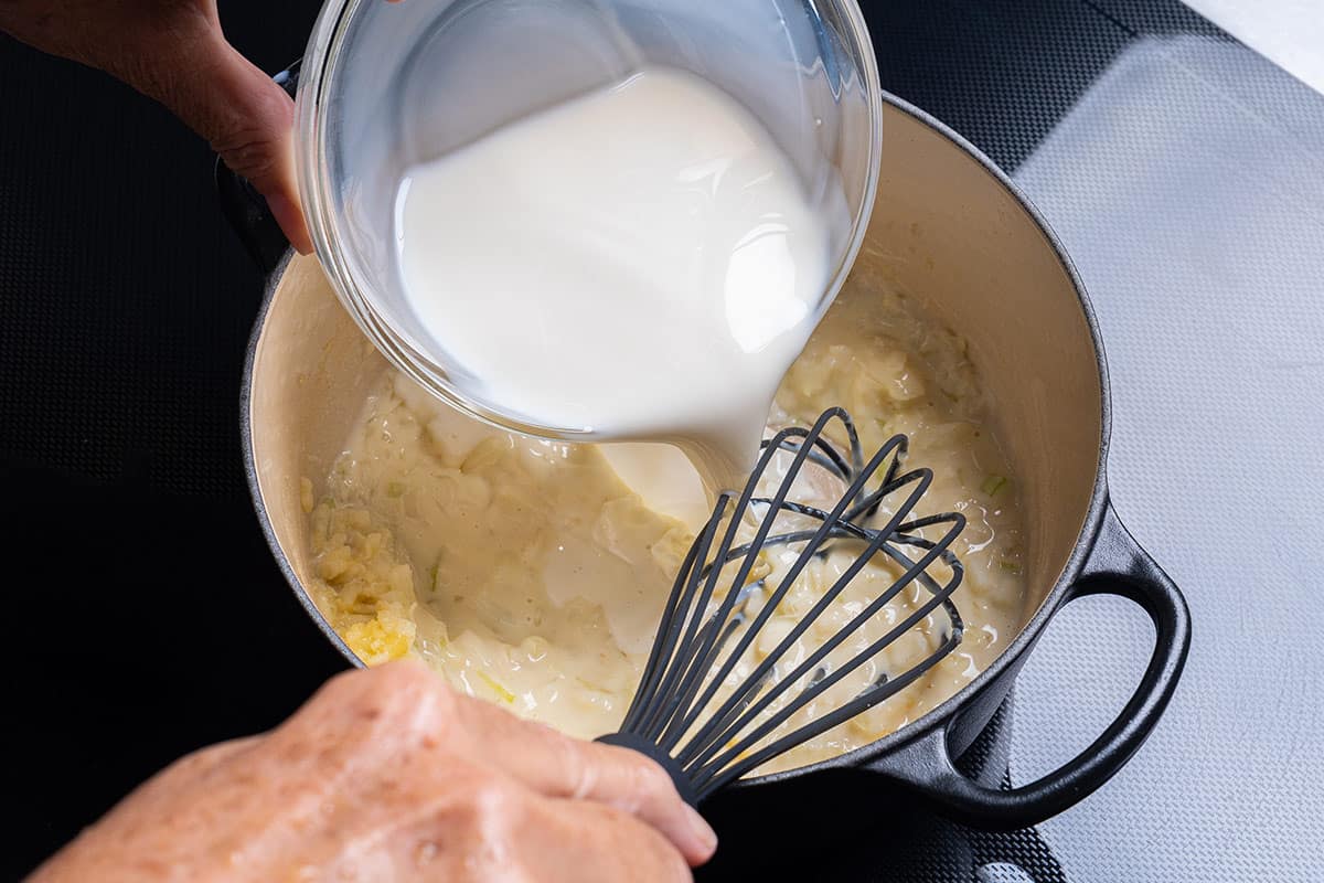 pot with flour, garlic and onion having milk poured in