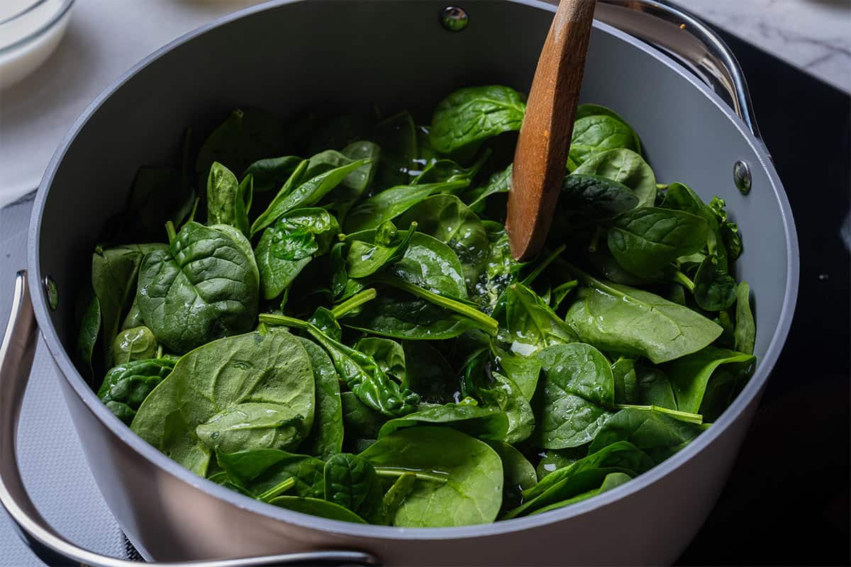pot with spinach and a wooden spoon touching the top