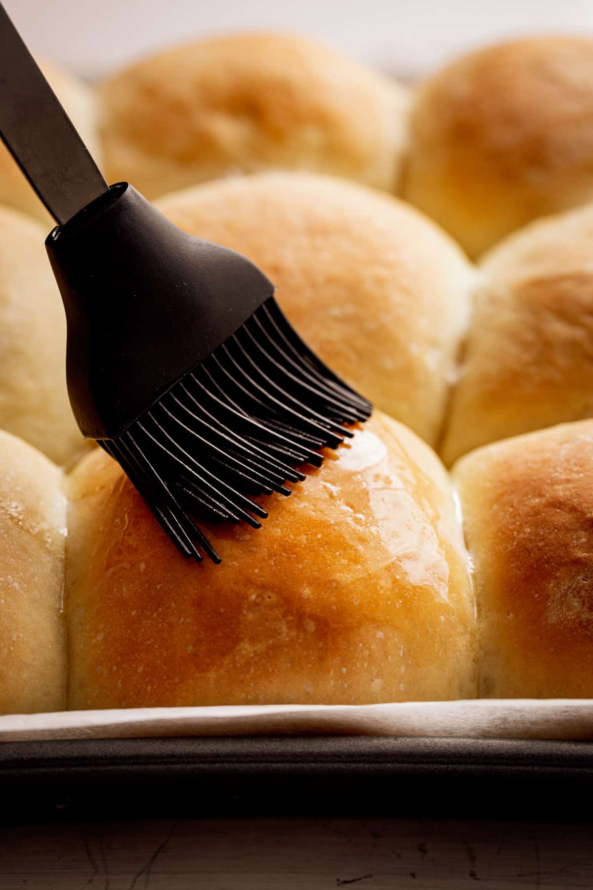 Golden dinner rolls being glazed with melted butter. 