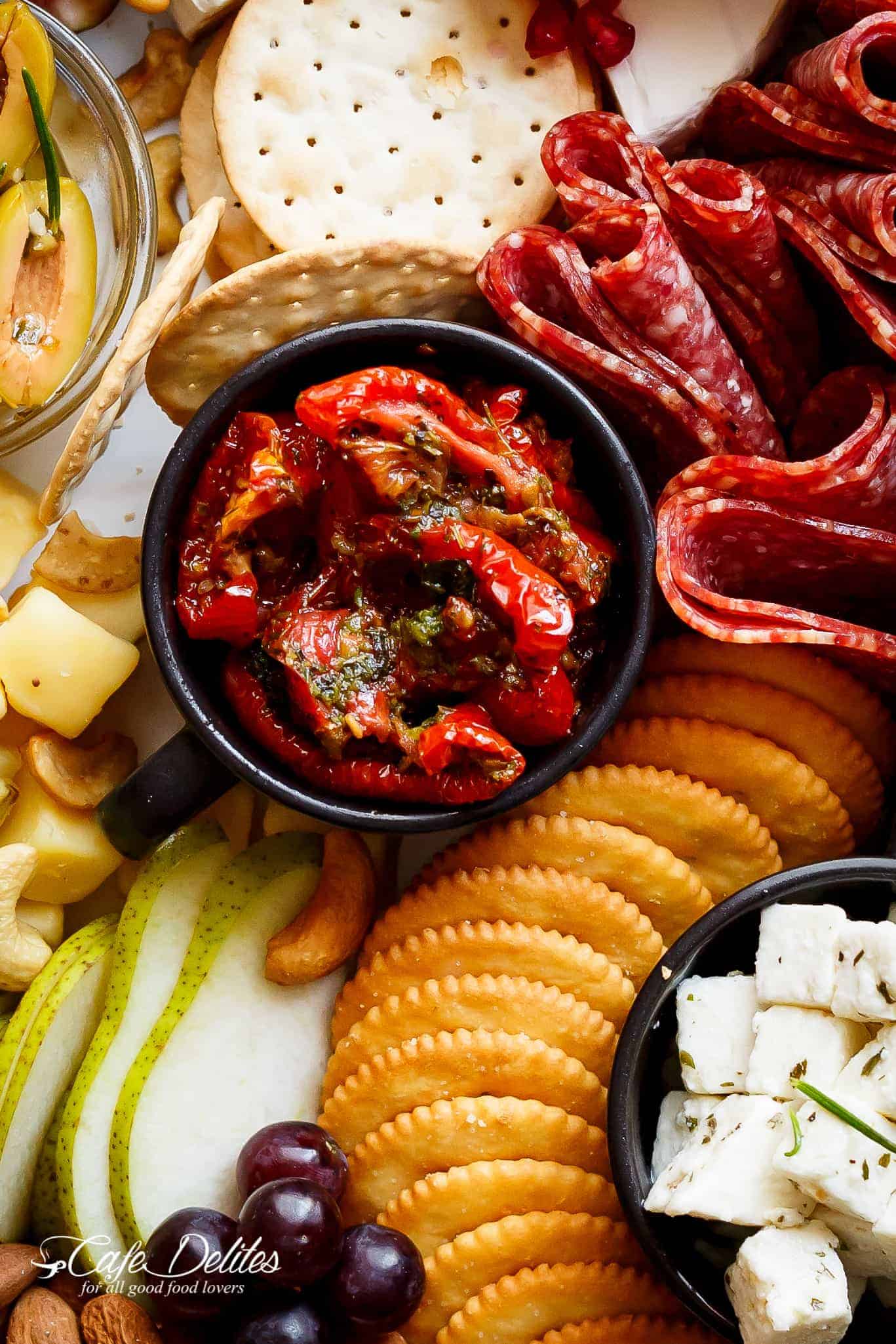 Close up of a ramekin of sun-dried tomatoes among other charcuterie items.