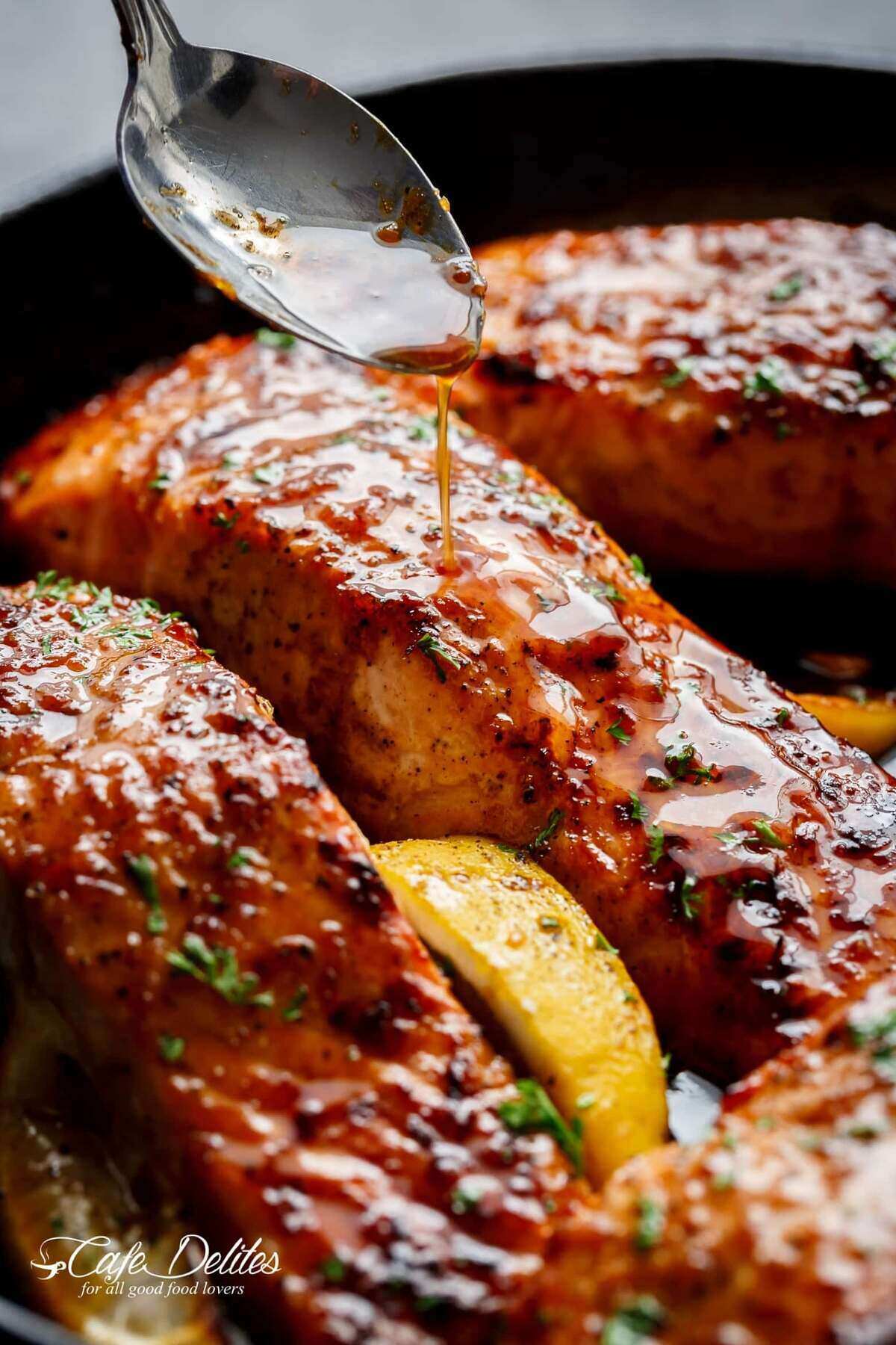 An amazing close-up shot of the salmon fillets coated in honey garlic sauce, sprinkled with basil, and accompanied by a slice of lemon.