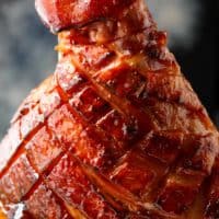 This close-up shot showcases a beautifully glazed ham, its surface glistening with a rich, caramelized coating. The ham has been meticulously scored in a diamond pattern, allowing the glaze to penetrate the meat and create tantalizing crevices of flavor. The deep, reddish-brown hue suggests a savory and slightly sweet profile. A generous amount of glaze pools around the base, inviting you to savor its deliciousness. The background is a dark gray, providing a neutral canvas that accentuates the ham's visual appeal.