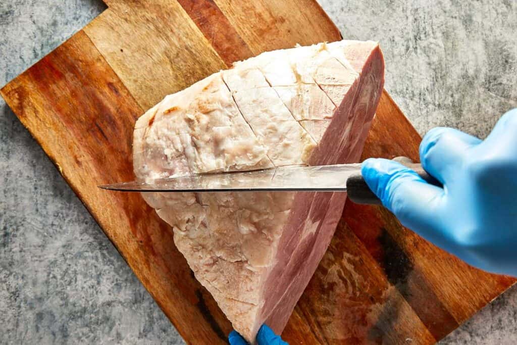 a knife cutting the ham into a diamond shape on a wooden board sitting on top of kitchen bench - 8